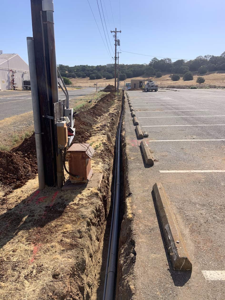 Conduit for electrical lines laying in open trench between road and parking lot