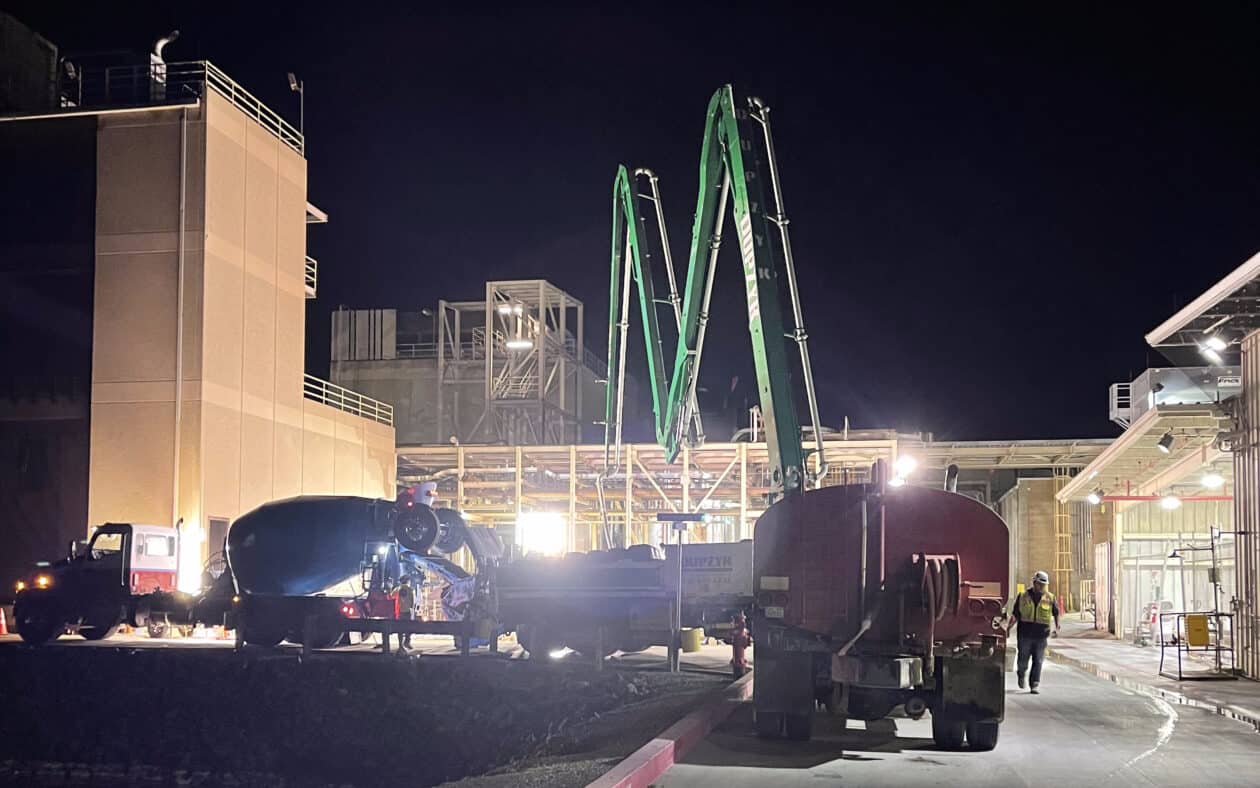 Concrete mixer truck supplying mud to pump truck for large industrial foundation job, with water truck in foreground